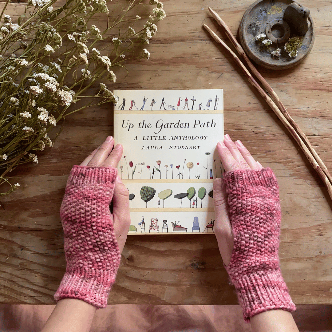 Two hands wearing knitted fingerless mitts holding a book