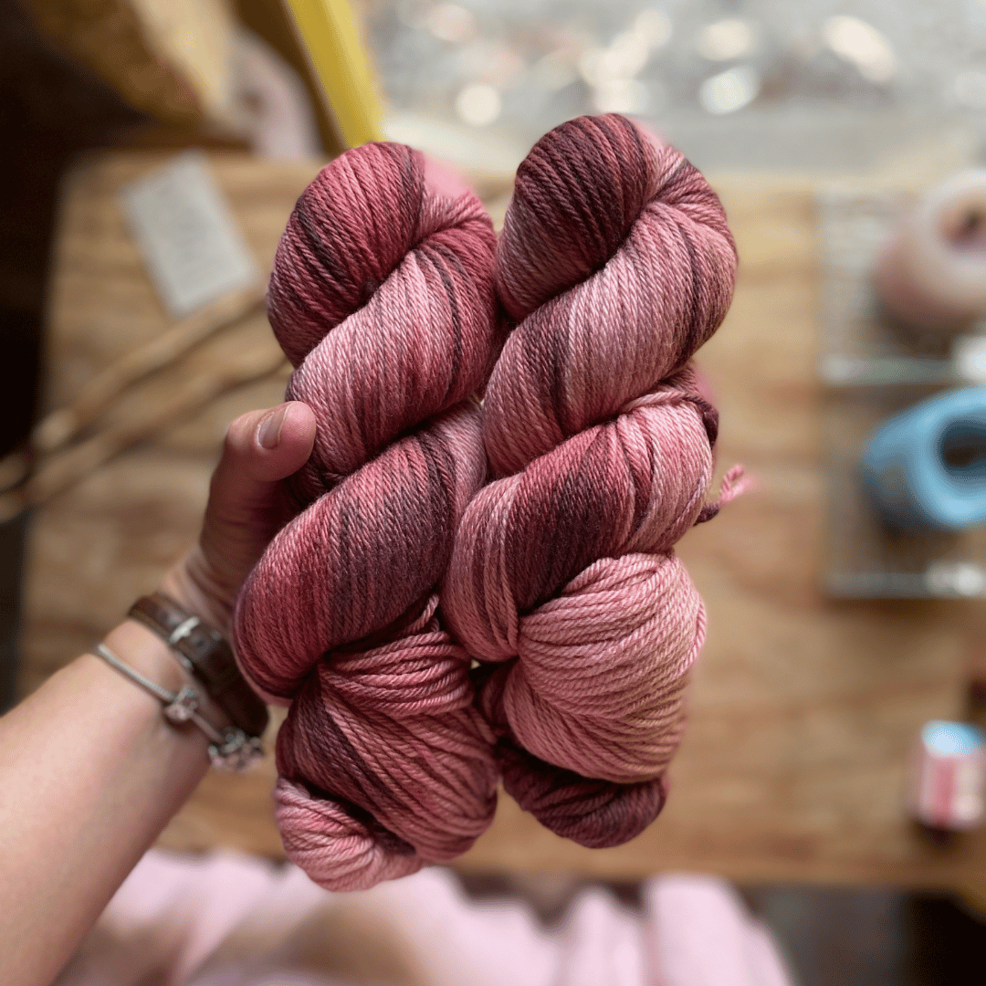 Two skeins of hand dyed yarn held in a hand, dyed by Augustbird.