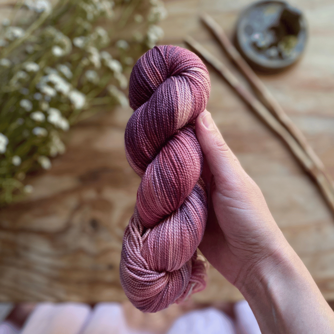 A skein of hand dyed yarn held in a hand, dyed by Augustbird.
