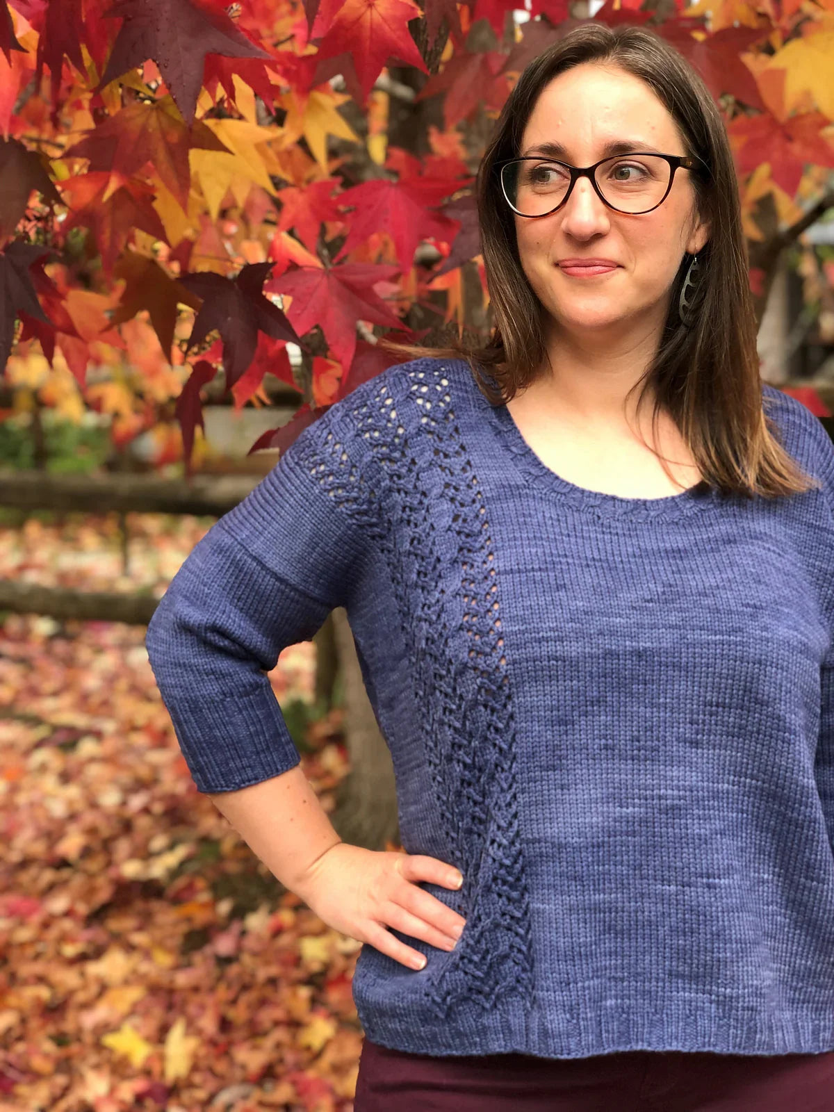 Woman wearing a hand-dyed indigo blue knit sweater with lace detail, autumn red and yellow leaves background