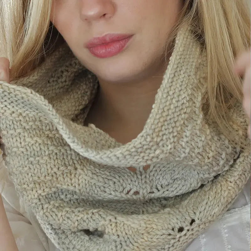 Close-up of woman wearing hand-dyed neutral beige knitted cowl scarf, showcasing soft textured yarn