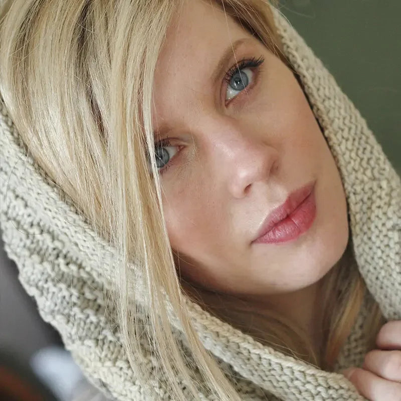 Close-up of woman with blue eyes wearing soft cream hand-dyed yarn knit hood from Augustbird