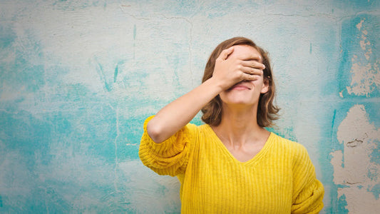 Person in yellow sweater covering eyes with hand against textured blue wall