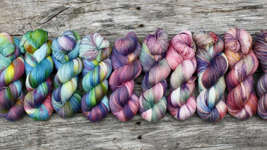 Hand-dyed colorful yarn skeins in pastel and vibrant shades arranged on rustic wooden surface