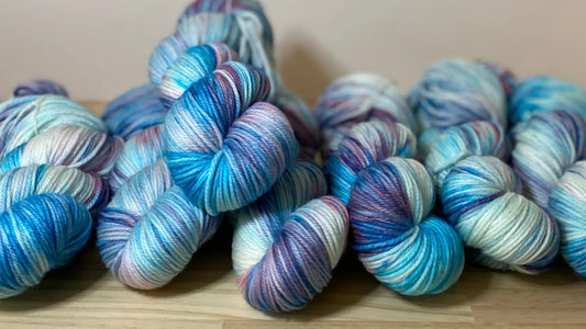 Hand-dyed yarn skeins in blue, purple, and white tones arranged on a wooden surface