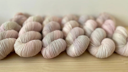 Hand-dyed soft yarn skeins in pale pastel pink arranged on a wooden surface