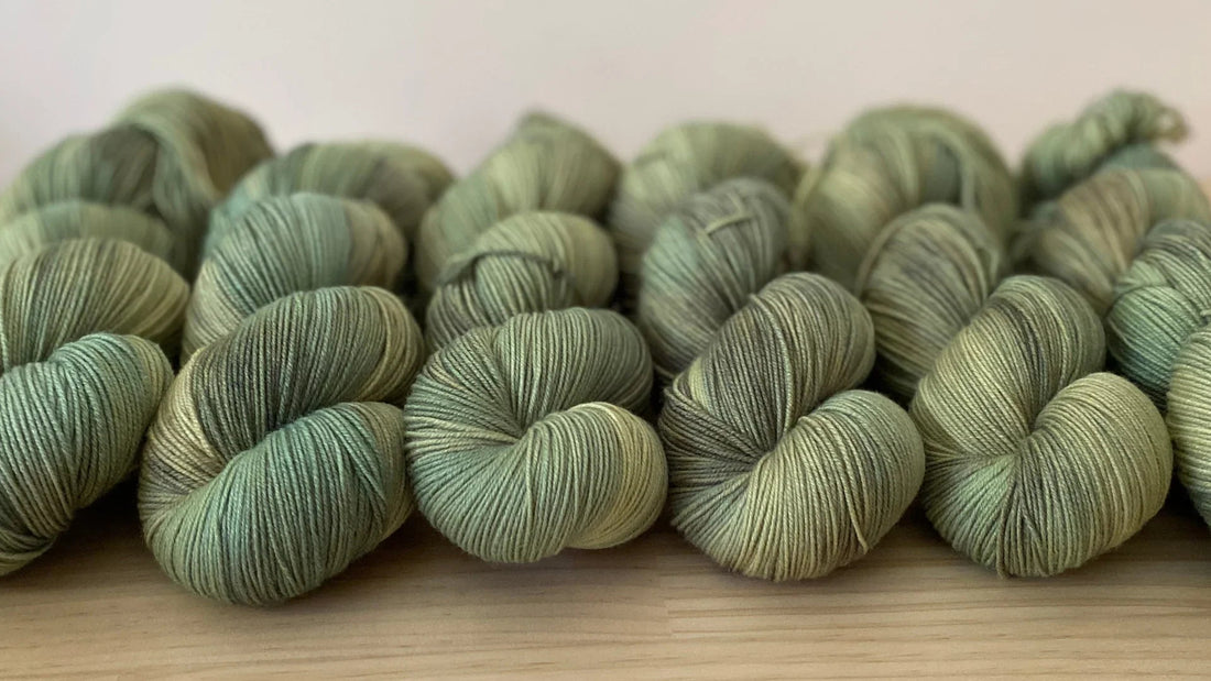 Hand-dyed soft yarn skeins in muted green shades neatly arranged on wooden surface