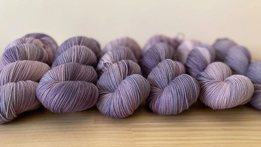 Rows of hand-dyed yarn skeins in soft mauve and purple shades on a wooden surface
