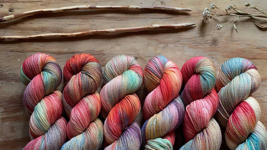 Six skeins of multicolored hand-dyed yarn on a wooden surface with dried flowers and sticks