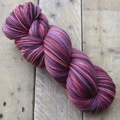 Hand-dyed skein of soft yarn with rich pink and purple tones on wooden surface from Augustbird