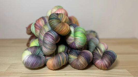 Pile of colorful hand-dyed yarn skeins on wooden surface with soft natural hues