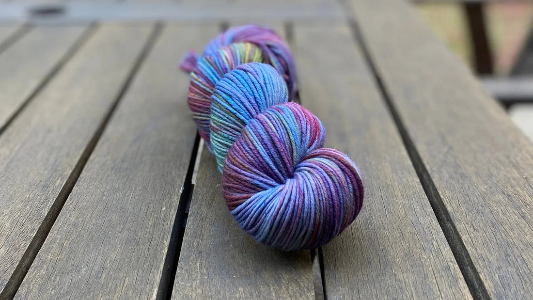 Hand-dyed colorful yarn skein with purples, blues, and greens on wooden table