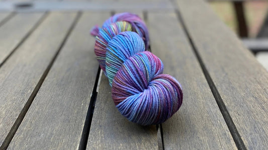 Hand-dyed colorful yarn skein with purples, blues, and greens on wooden table