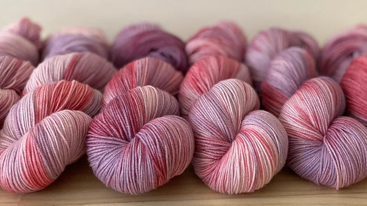 Hand-dyed yarn skeins in soft pink and purple tones arranged on a wooden surface