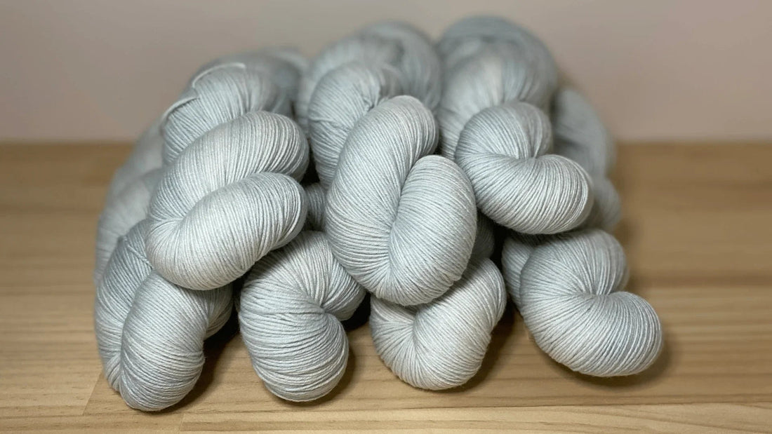 Hand-dyed soft grey yarn skeins stacked on wooden surface by Augustbird
