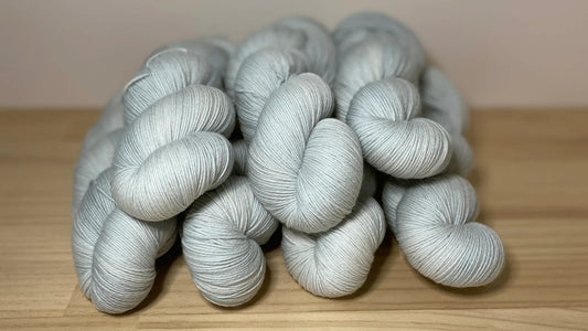 Hand-dyed soft grey yarn skeins stacked on wooden surface by Augustbird