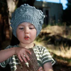 Child wearing a hand-dyed grey knit winter hat outdoors, holding a piece of wood in natural light