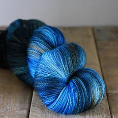 Hand-dyed Ashmore 4ply yarn in blue and green hues on wooden surface by Augustbird