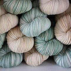 Close-up of hand-dyed soft yarn skeins in muted green and beige tones, showcasing artisanal quality by Augustbird