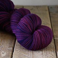 Hand-dyed soft yarn in deep purple and pink shades on rustic wooden surface, Augustbird artisanal yarn