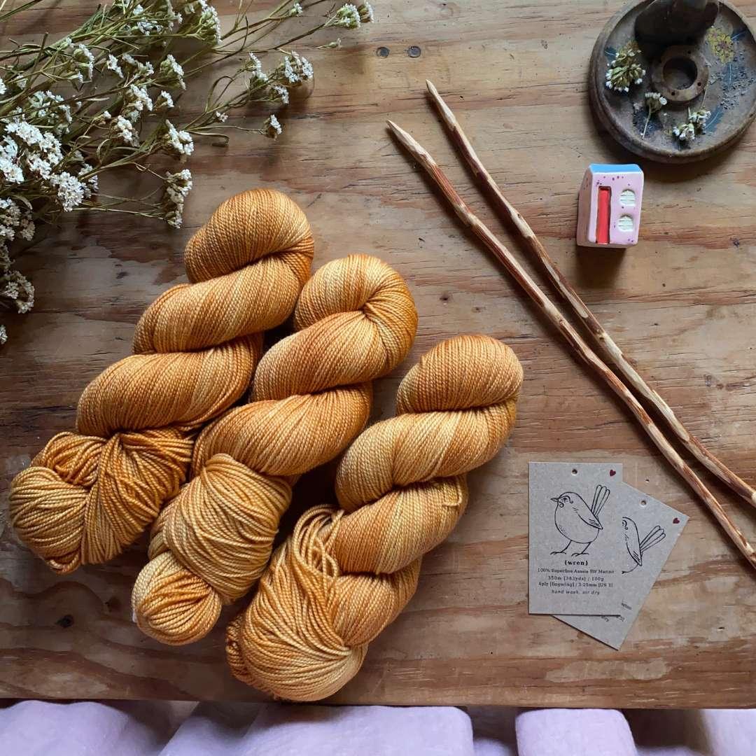 Hand-dyed golden yellow yarn skeins on wooden table with natural wooden knitting needles and dried flowers