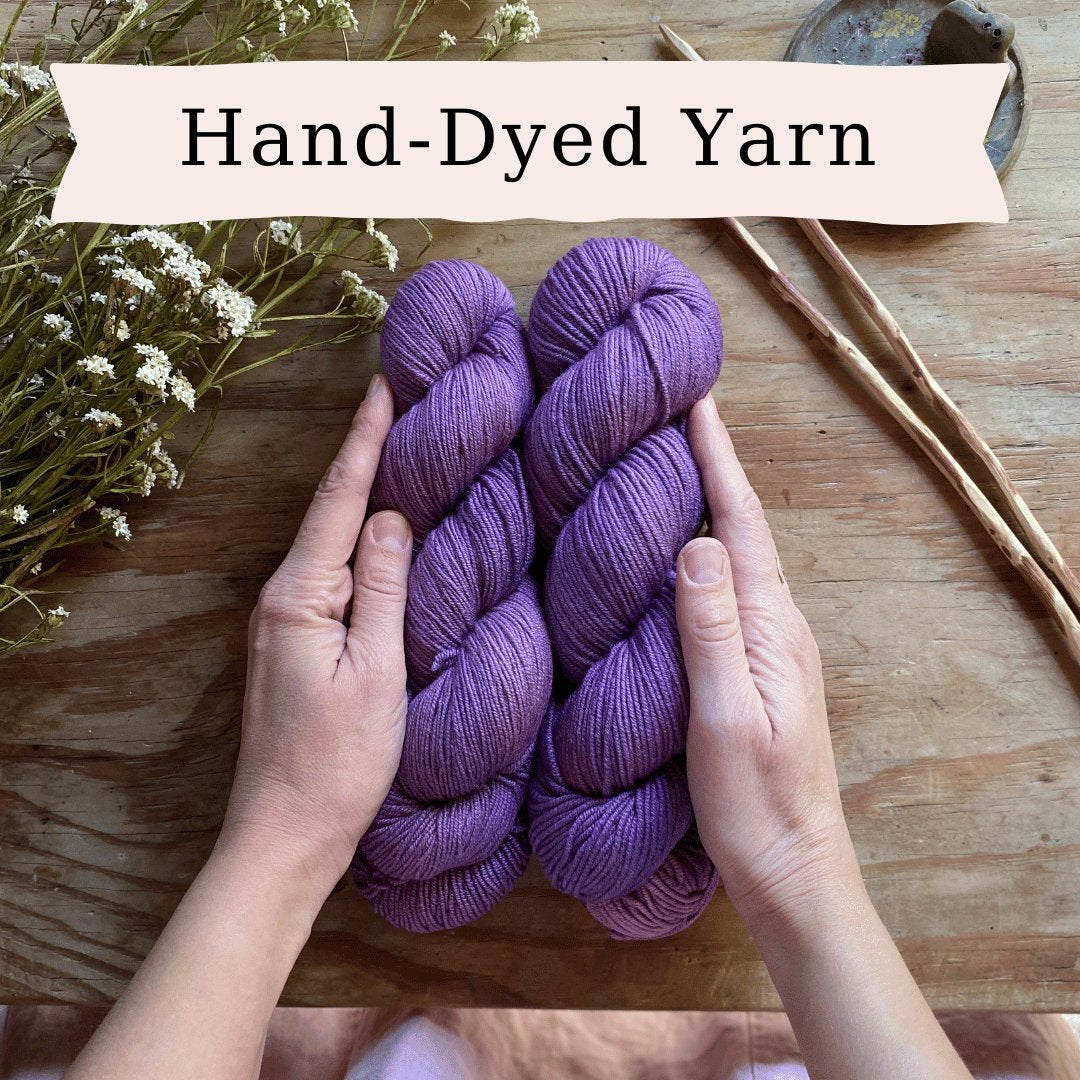 The words Hand Dyed Yarn and with two hands holding two skeins of purple hand dyed yarn.