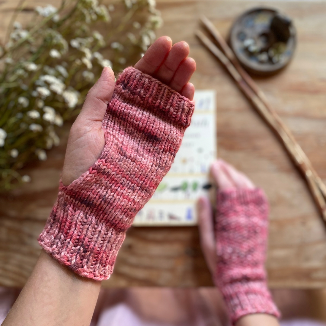 Two hands, wearing fingerless knitting mitts. One help up close to the camera. 