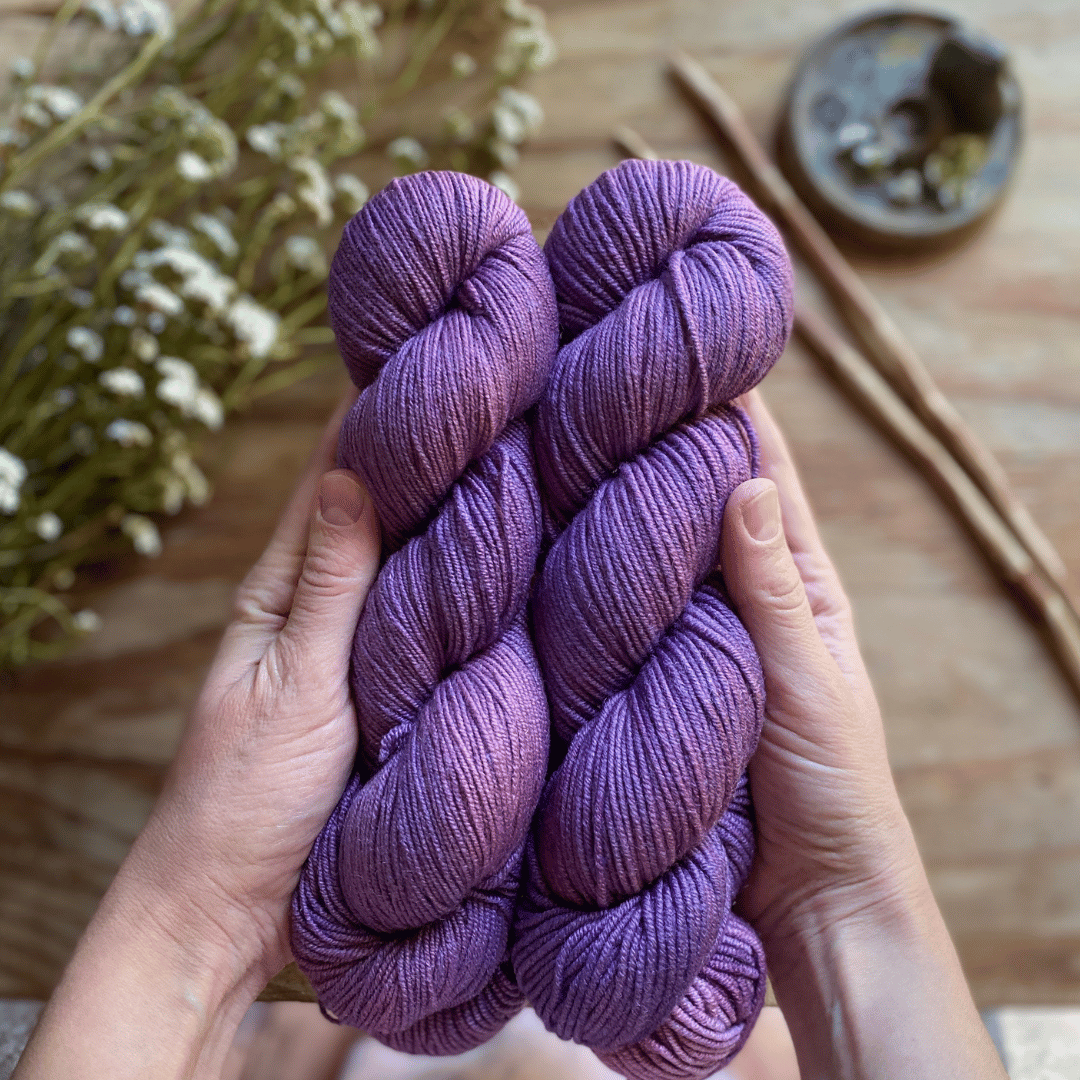 Two skeins of purple hand-dyed yarn held in two hands.
