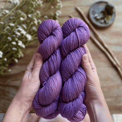 Two skeins of purple hand-dyed yarn held in two hands.