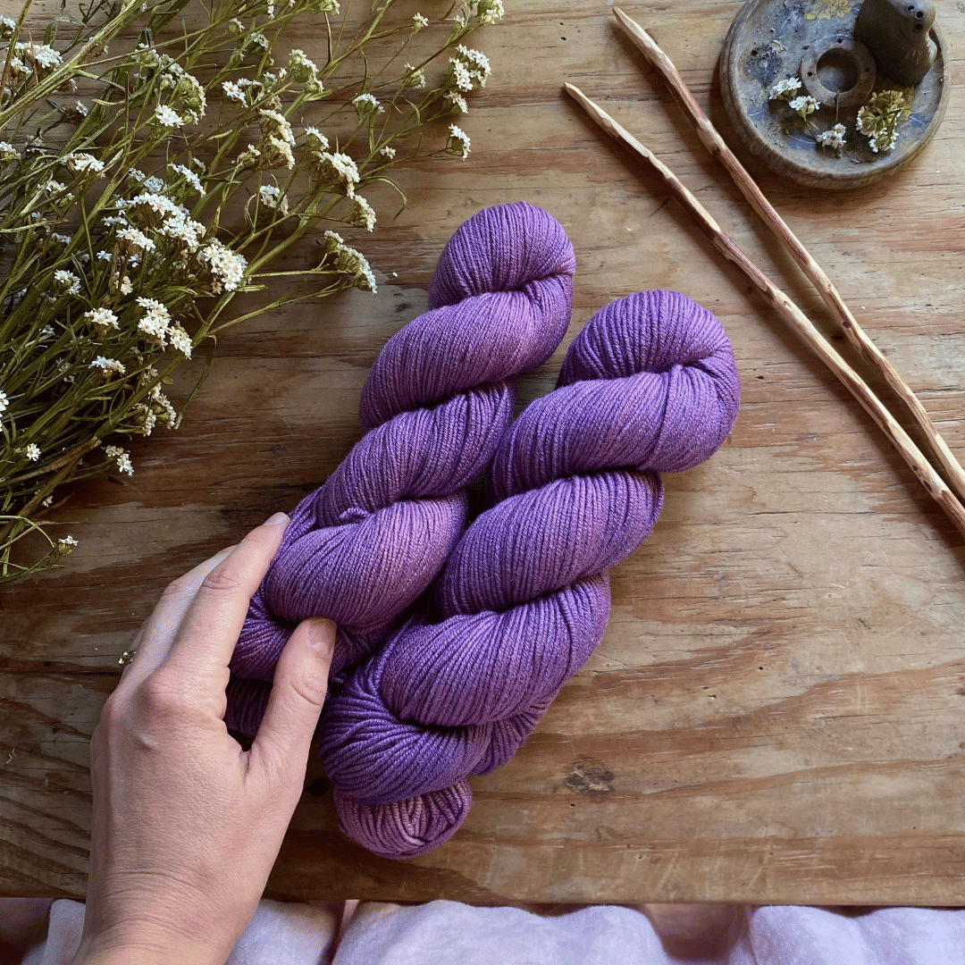 Two skeins of purple hand-dyed yarn on a wooden table.