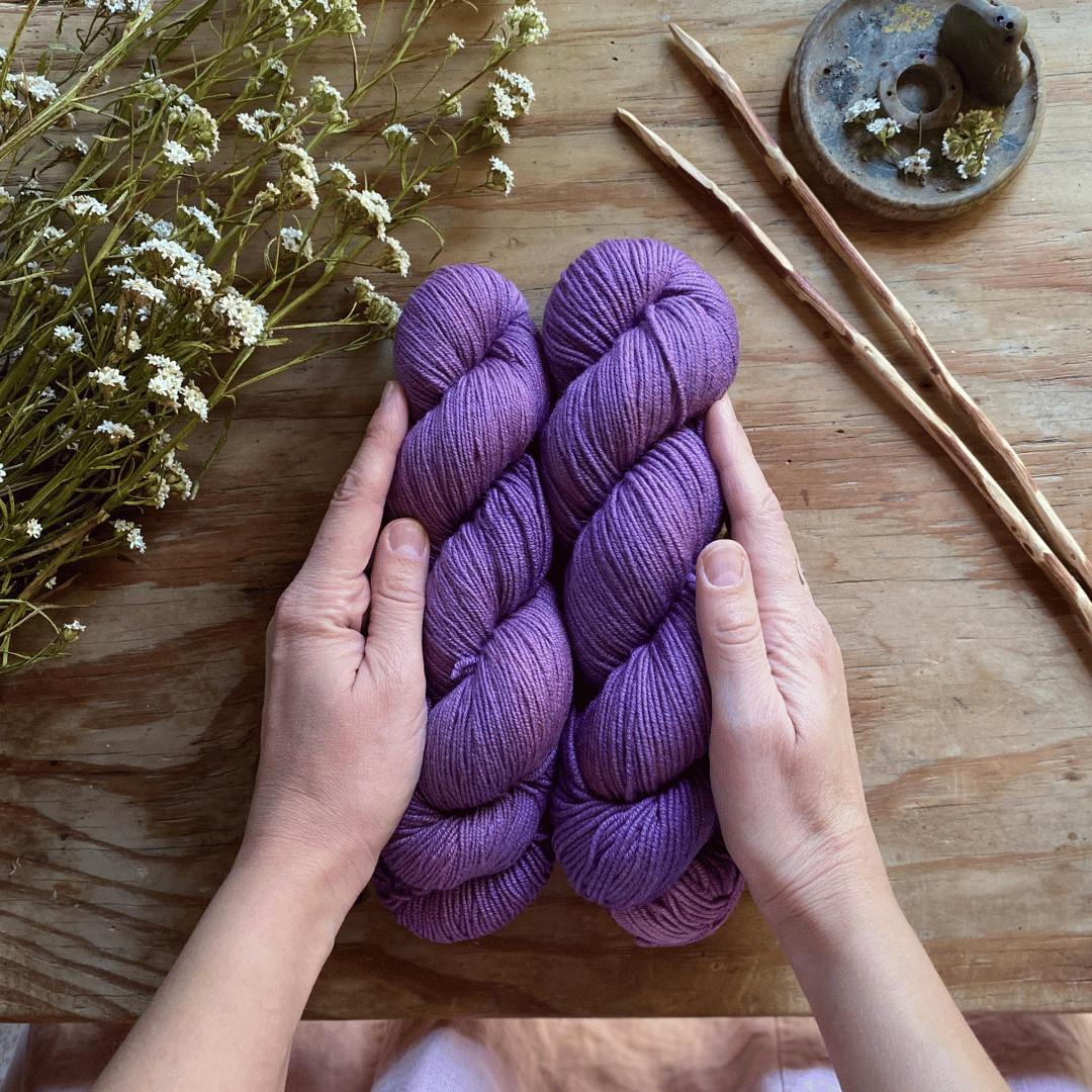 Two skeins of purple hand-dyed yarn on a wooden table.