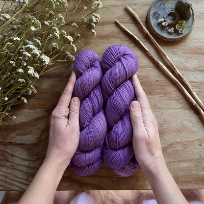 Two skeins of purple hand-dyed yarn on a wooden table.
