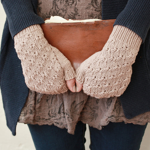 A close up of a woman's hands, wearing knitted fingerless mitts and holding an old book. 