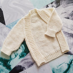 White frontless baby cardigan on a mixed marble collage.