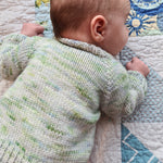 Close up of a baby from the back wearing a 'baby vertebrae' in hand dyed yarn.