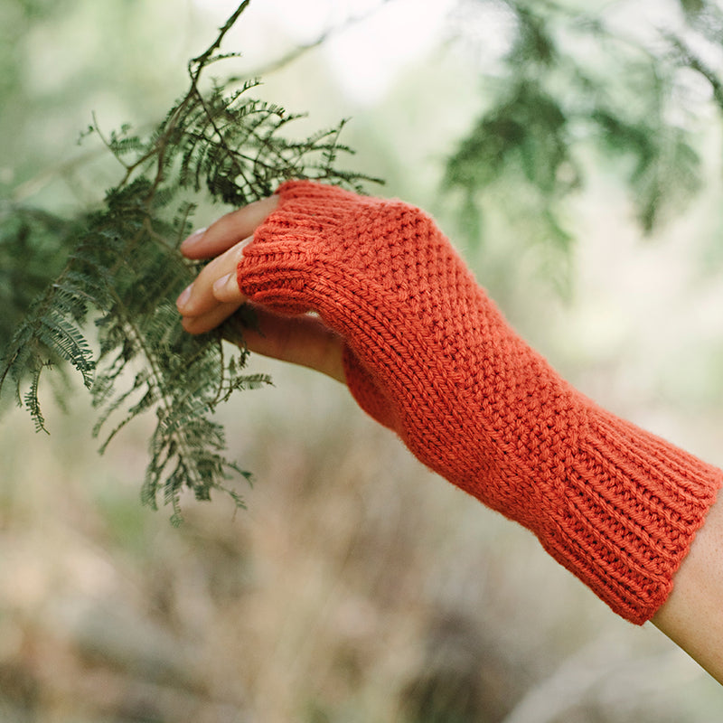 close up of one hand wearing fingerless mitt, picking leaves